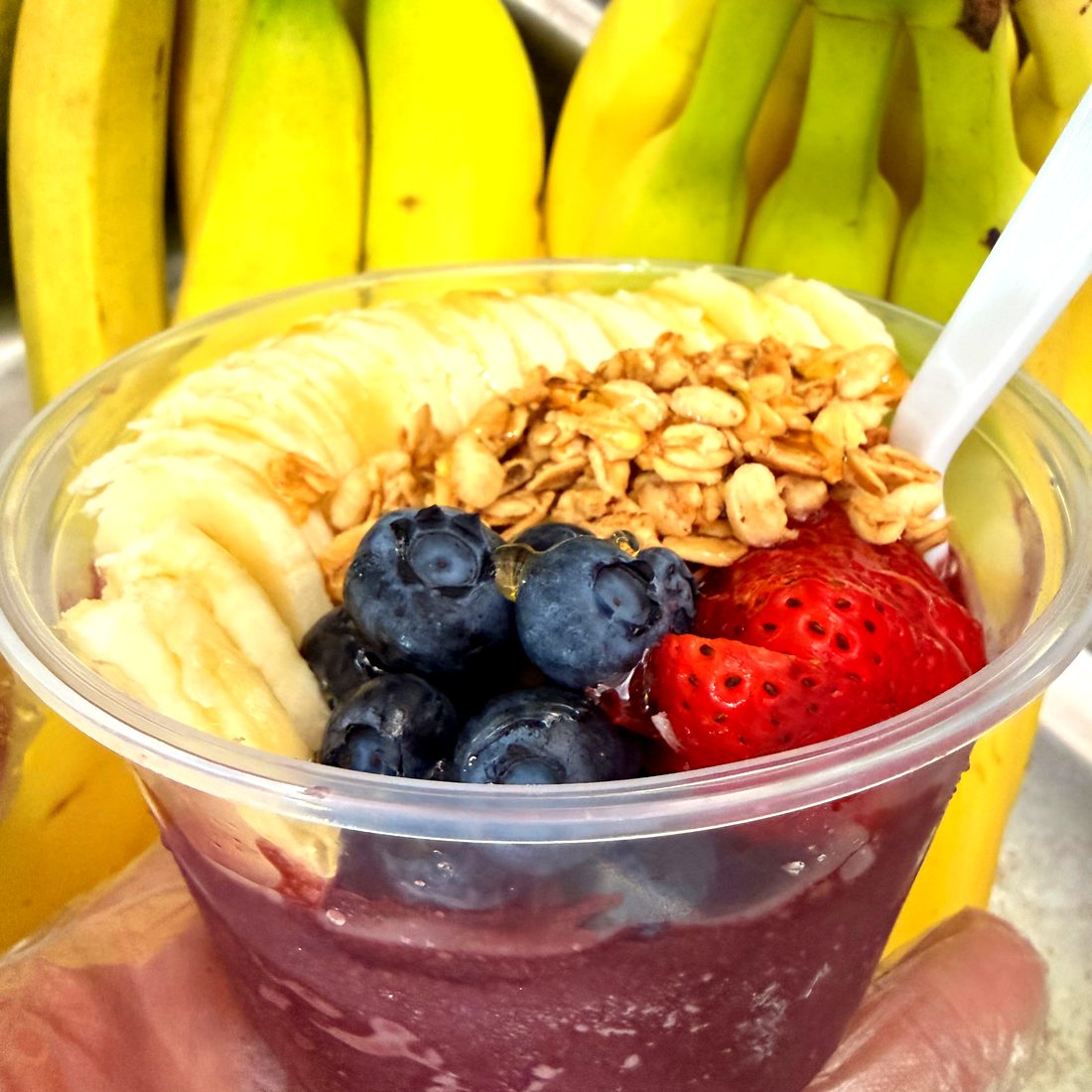 Açaí bowl held up with fresh bananas behind